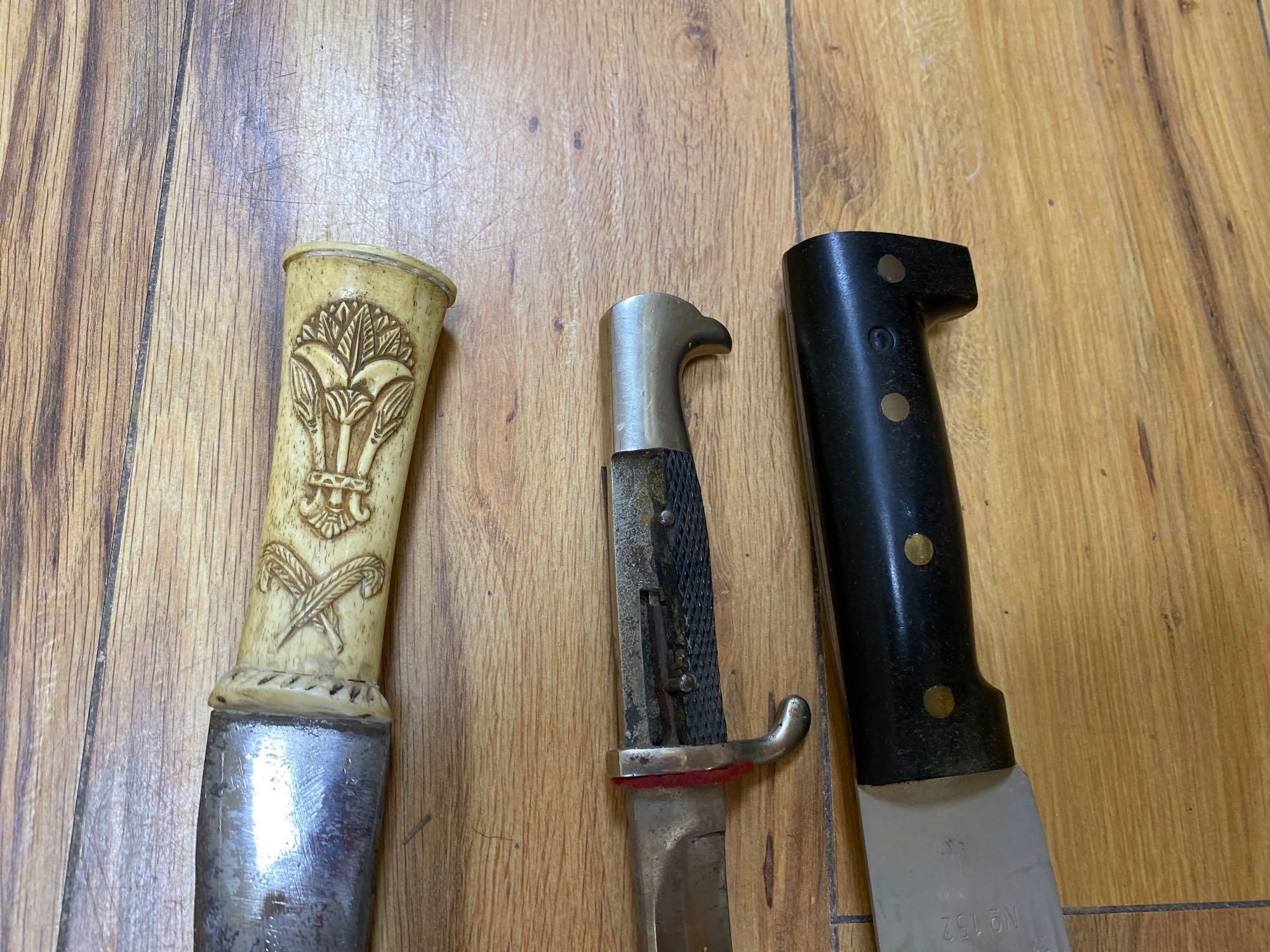 Five various weapons including a Kukri, a carved bone handled dagger with brass sun, moon and stars sheath and an El Salvador machete